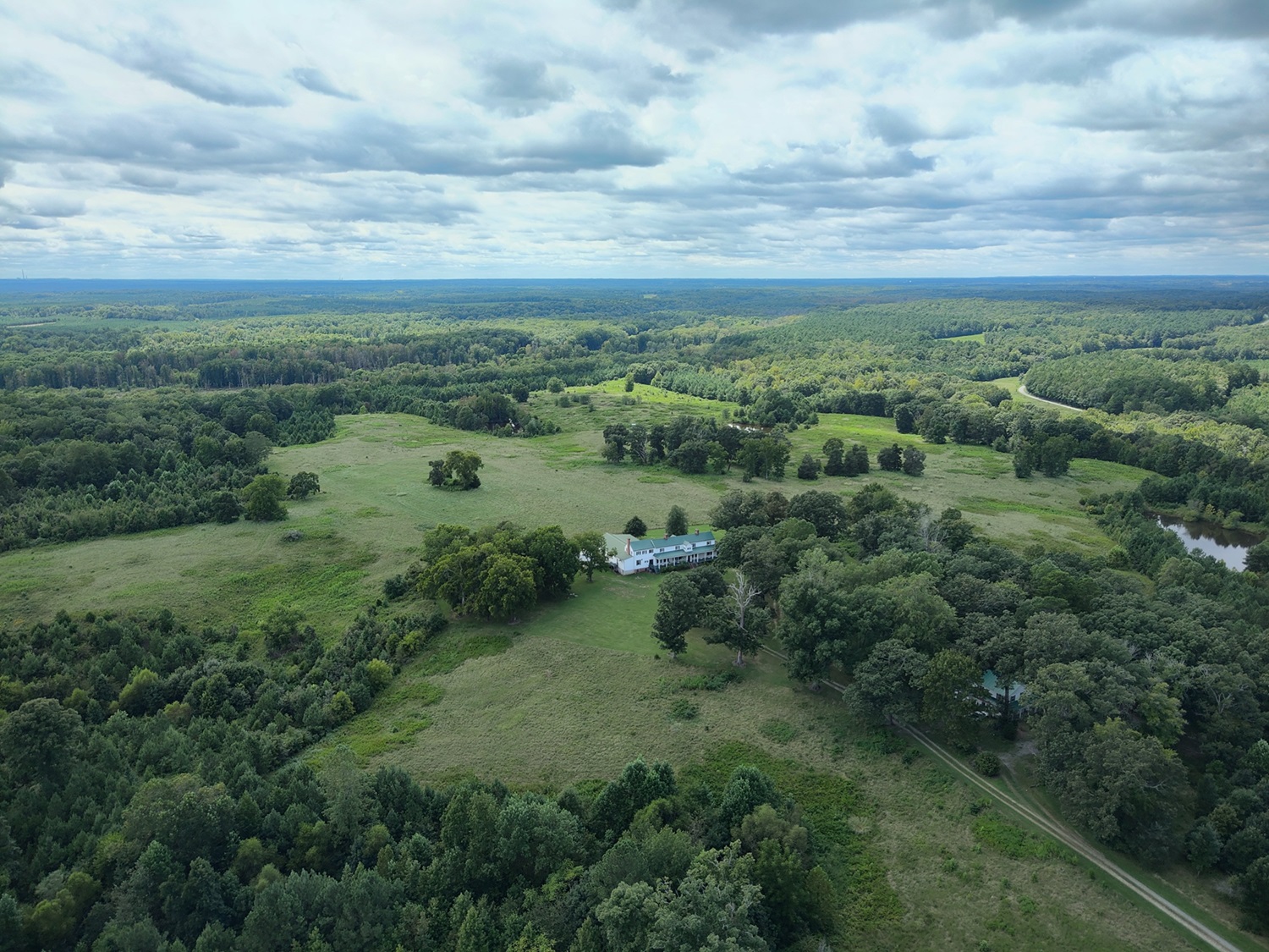 Photo of Falkland Farms property showing a white farmhouse with a green roof and red chimneys in an open area dotted with patches of trees.