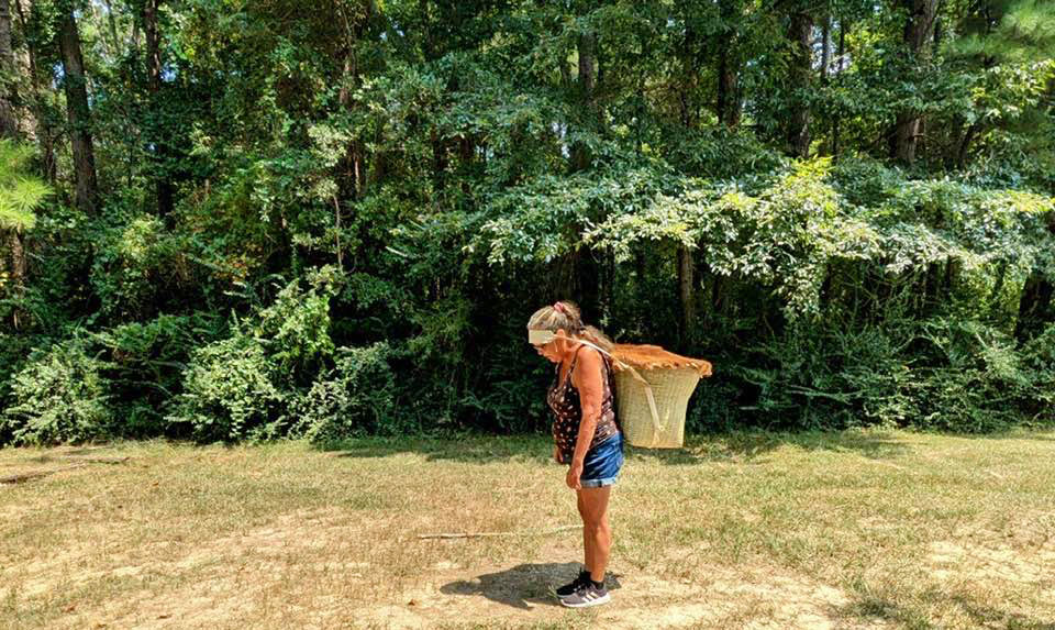 Photo of standing woman carrying a basket on her back.