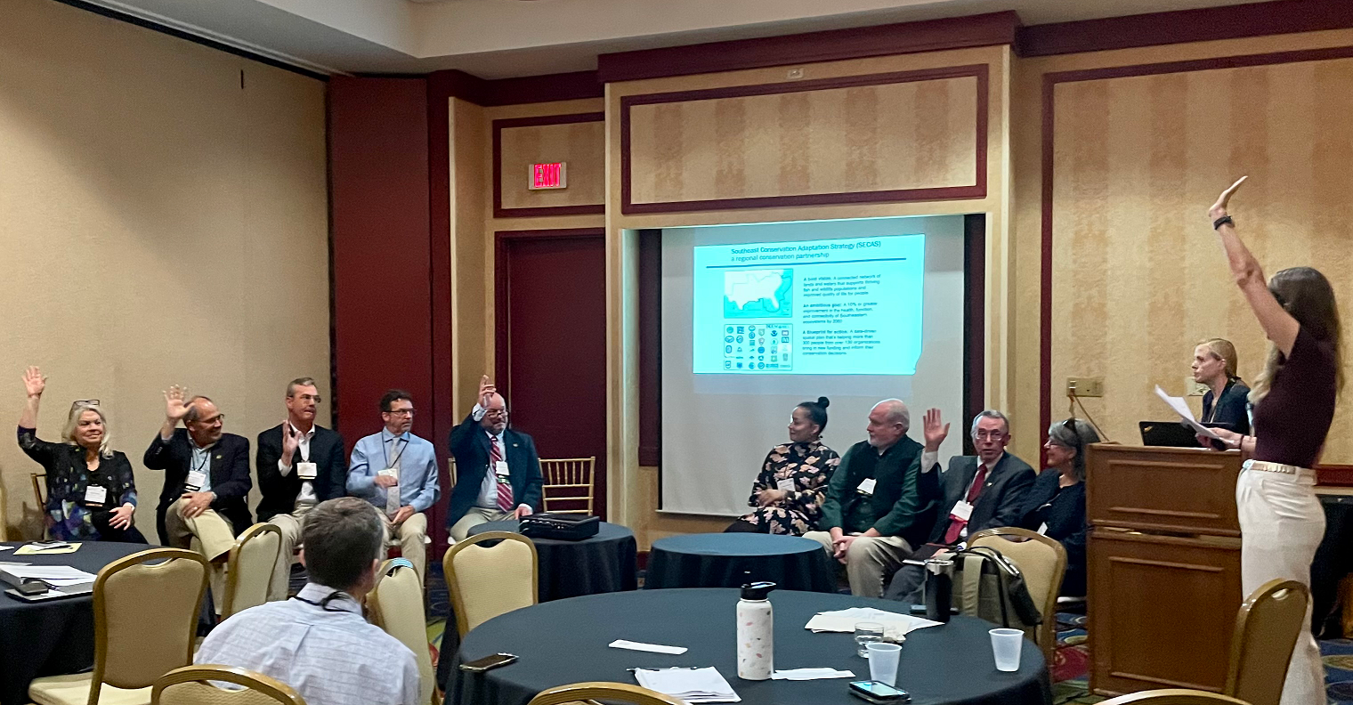 Photo from the SECAS symposium at the 2022 SEAFWA annual conference showing 9 members of SECAS executive-level leadership seated at the front of the room, engaged in a panel discussion.