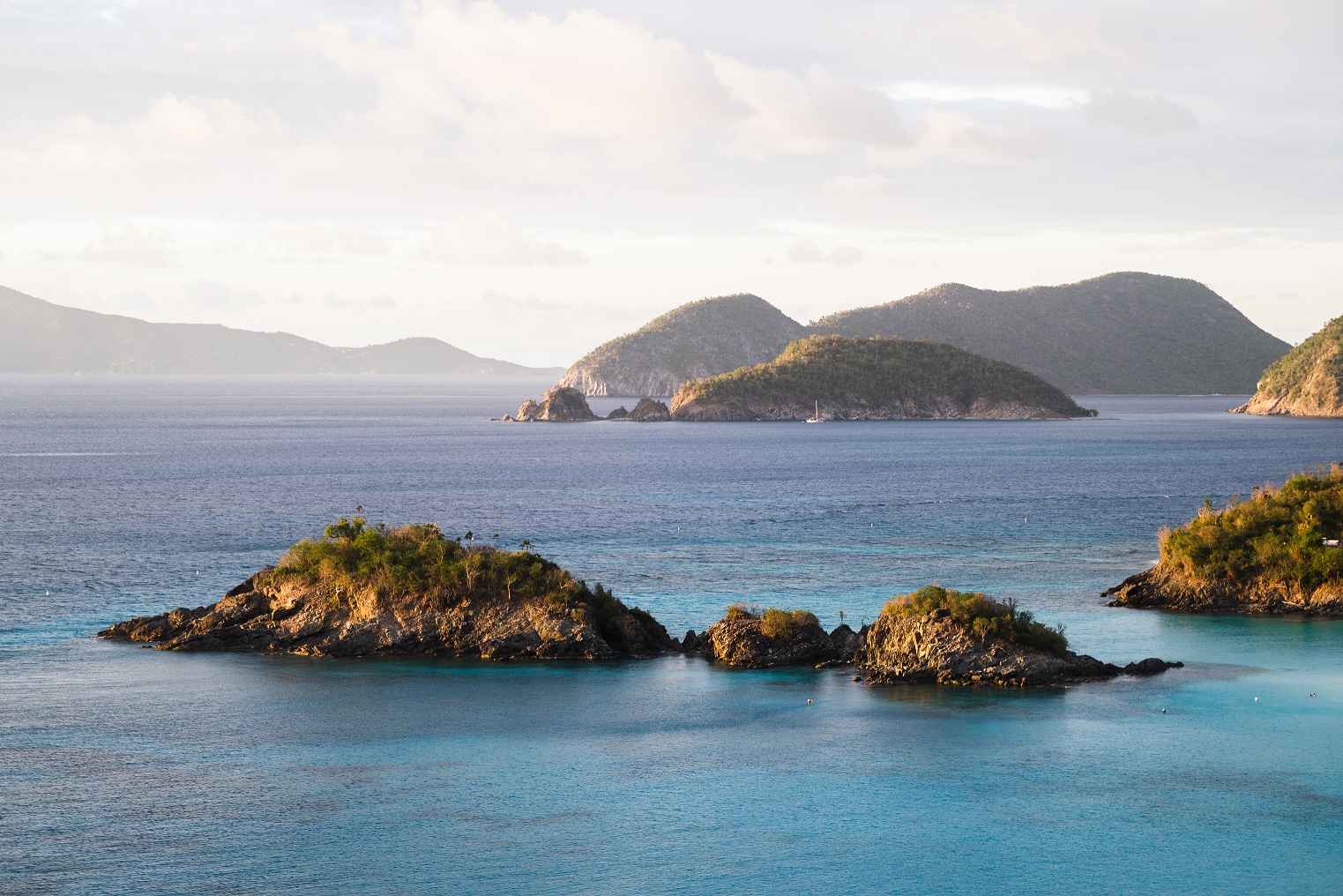 Ocean in shades of turquoise and darker blue with rocky islands in the background and foreground covered with scrubby green vegetation.