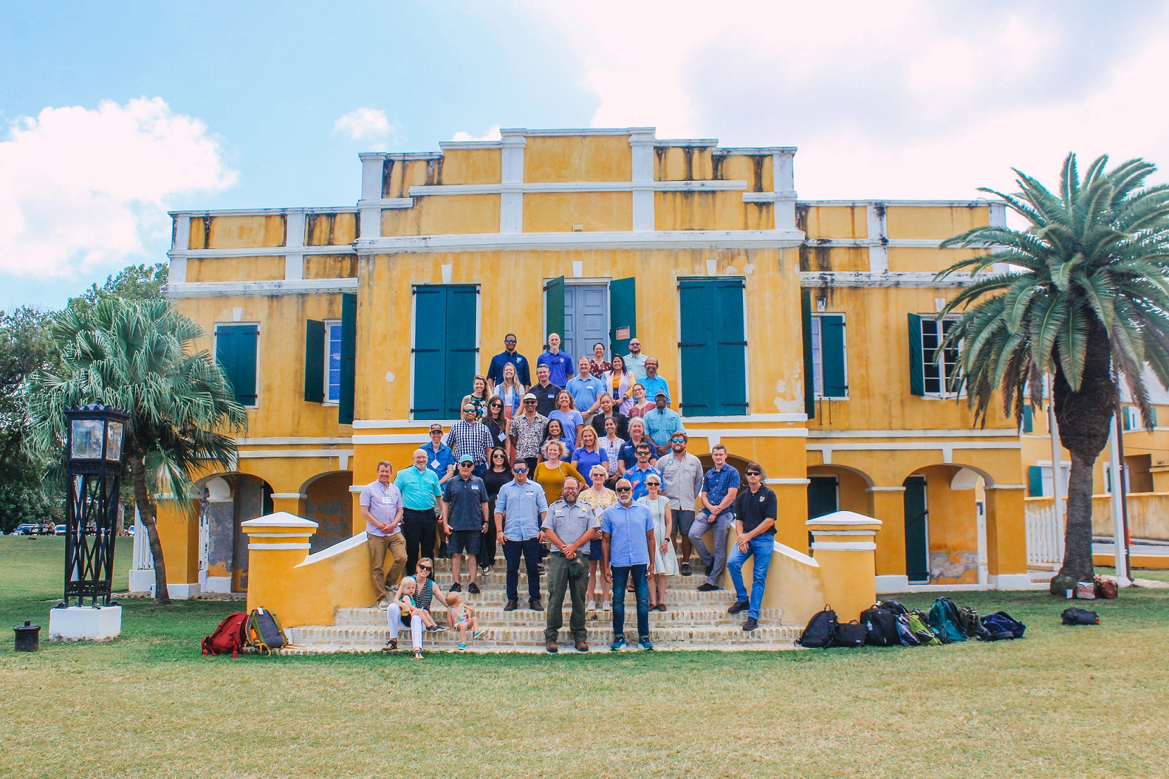 Group photo of meeting attendees standing on the front steps of a weathered yellow and white building.