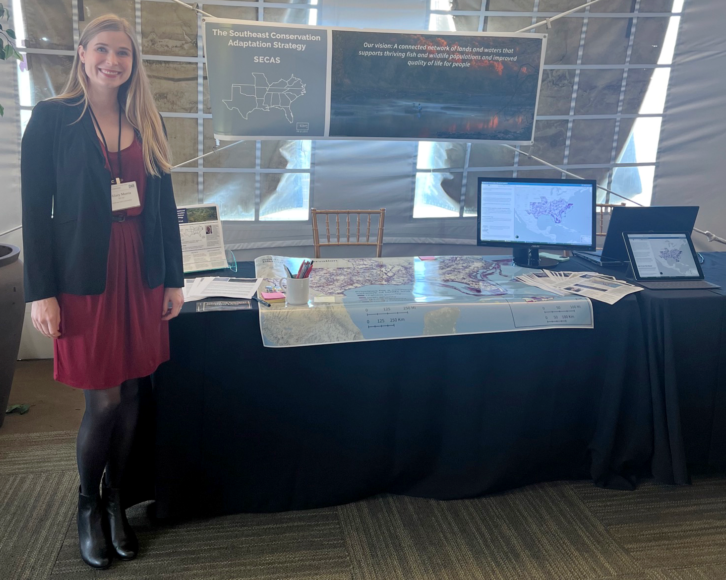 Hilary stands to the left of the SECAS exhibit booth at the 2022 SEAFWA annual meeting.