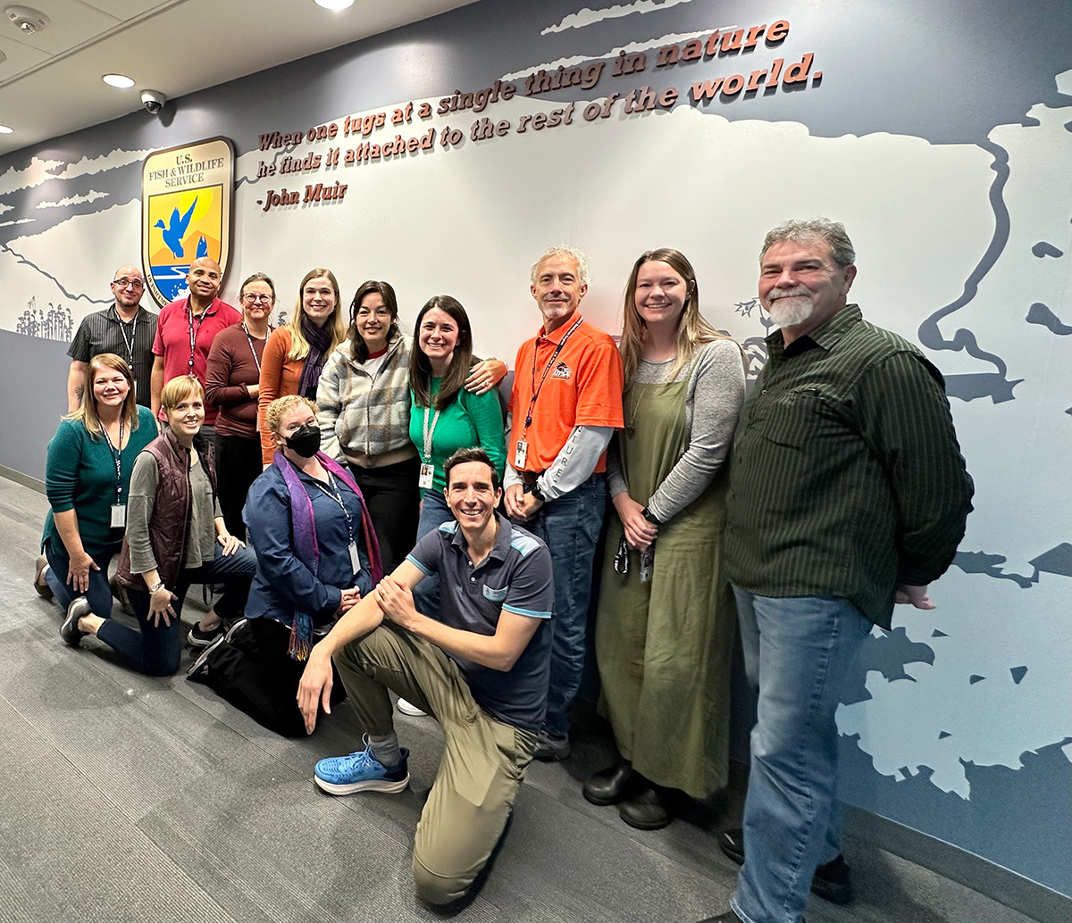 Photo of the SECAS staff team standing smiling under a quote by John Muir.