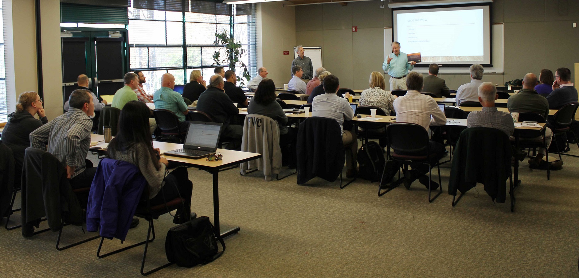 Meeting room filled with people in chairs facing a projector screen. Ed Carter, Executive Director of the Tennessee Wildlife Resources Agency, stands in front of the screen, presenting.